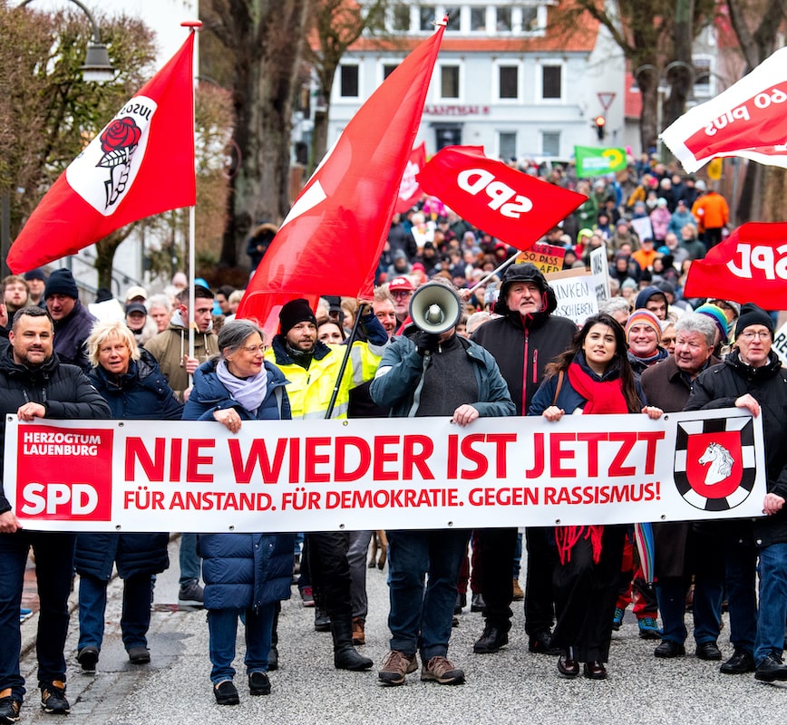 Foto: SPD-Mitglieder nehmen in Mölln an einer Demonstration gegen Rechtsextremismus unter dem Motto „Nie wieder ist jetzt“ teil, gehen über die Straße und halten Transparente