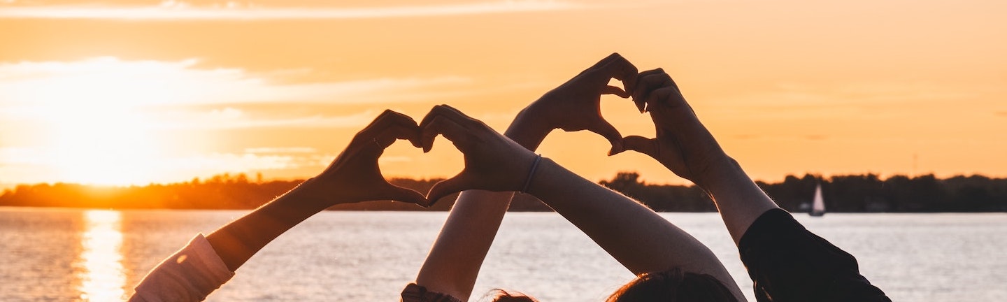 Foto: Junge Menschen bilden mit Händen Herzen vor Sonnenuntergang