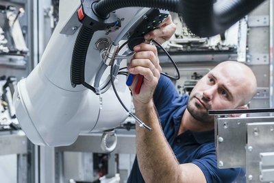 Foto: Mann arbeitet an einem Industrieroboter in einer modernen Fabrik 
