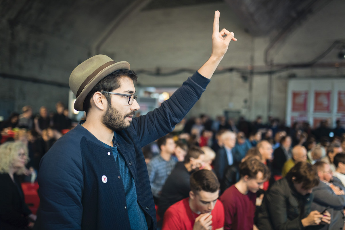 Foto: Junger Mann hebt beim Debattencamp 2018 Zeigefinger um eine Frage zu stellen