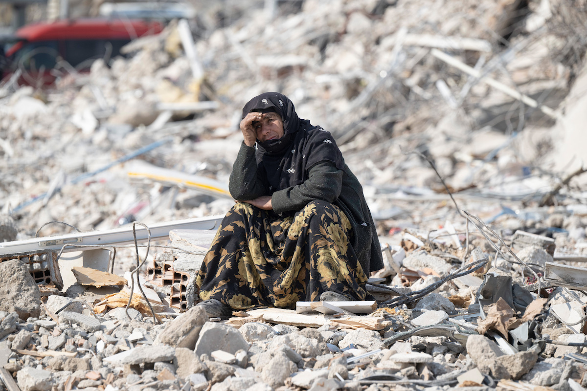 Foto: Eine Frau sitzt in Antakya zwischen den Trümmern.