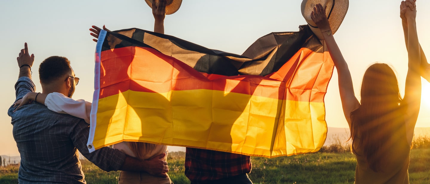 Foto: Junge Menschen mit Deutshcladnfahne jubeln bei Sonnenuntergang