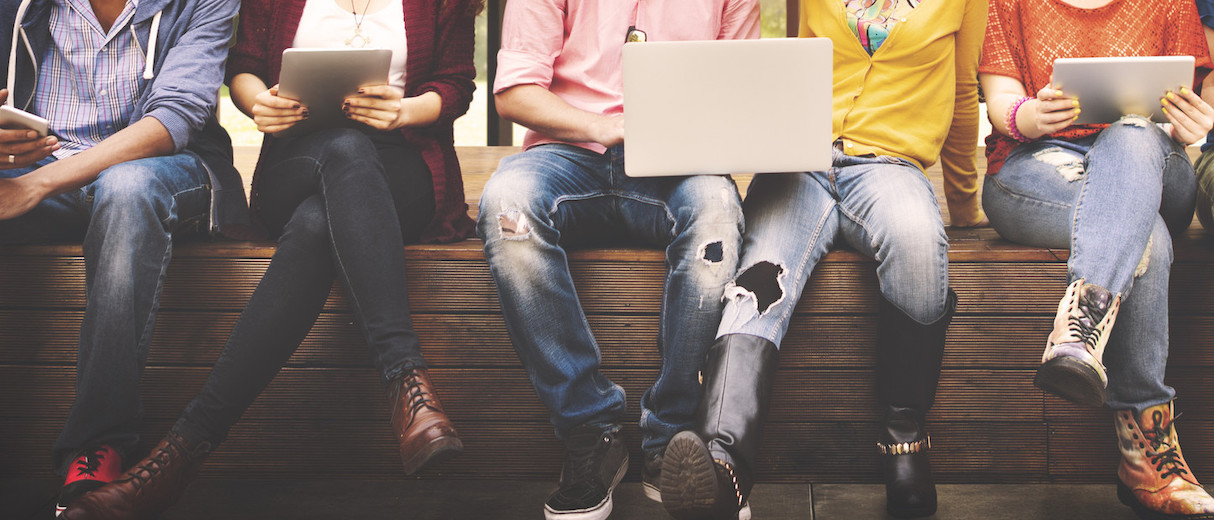 Foto: Junge Menschen sitzen nebeneinander und nutzen Handy sowie Laptops