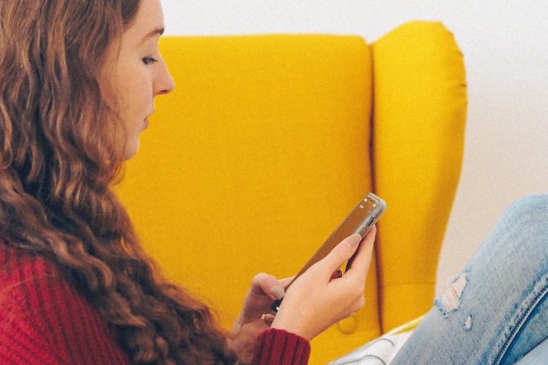 Foto: Frau sitzt auf Sofa und schaut auf ein Handy