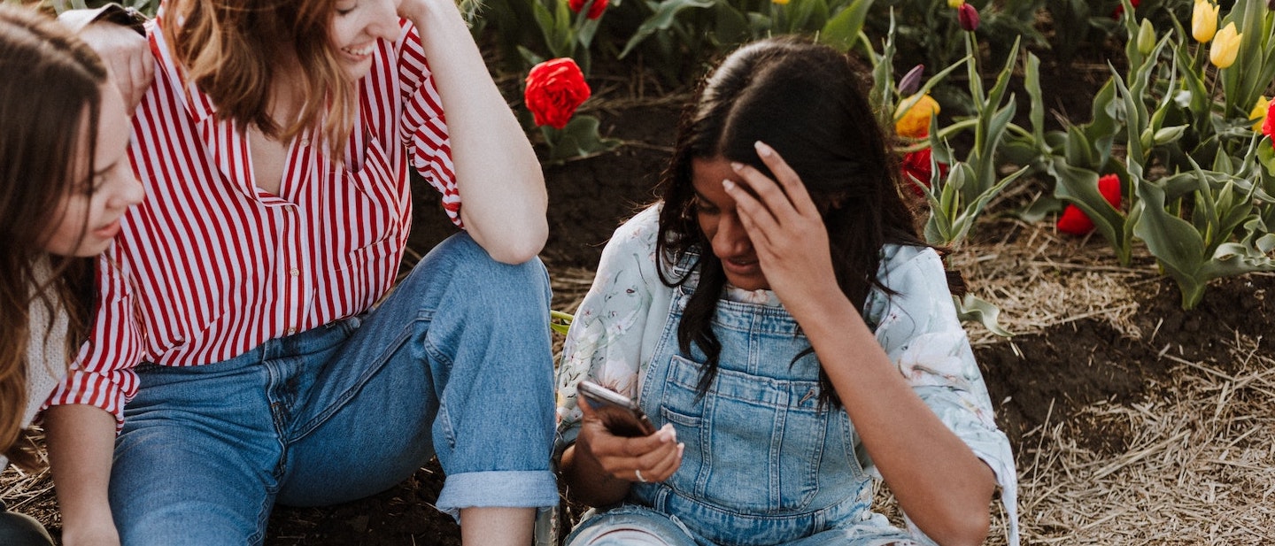 Foto: Drei junge Frauen unterhalten sich sitzend an einem Handy