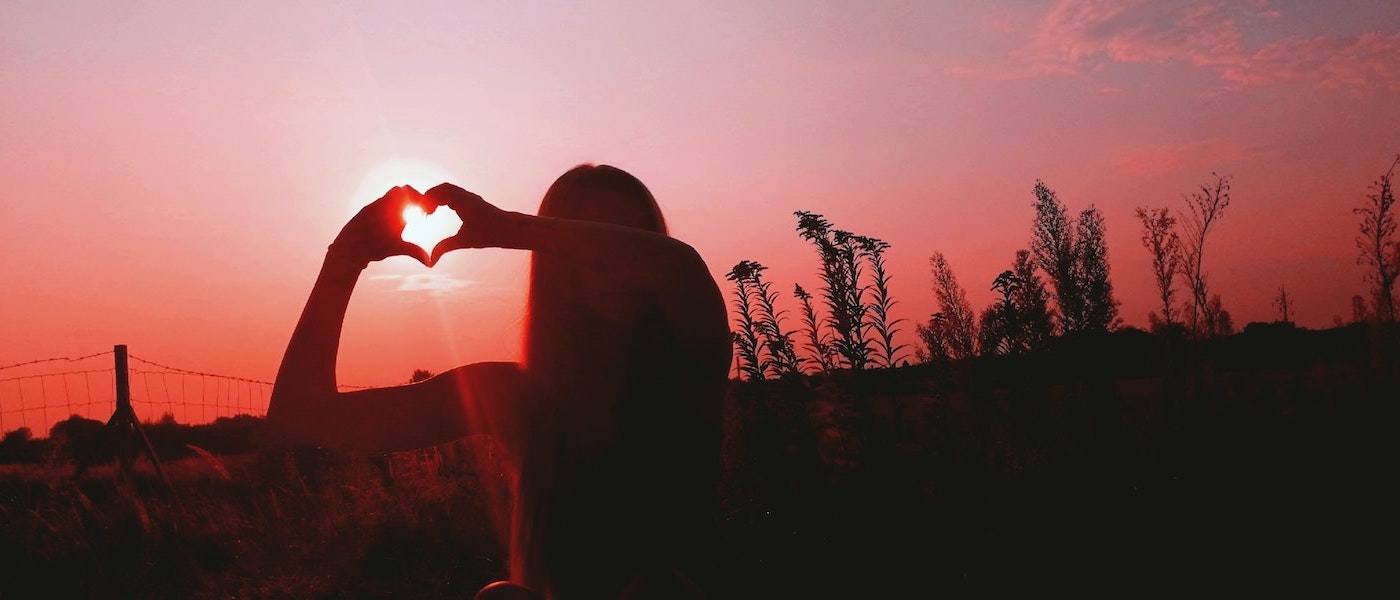 Foto: Frau bildet bei Sonnenuntergang mit Händen ein Herz
