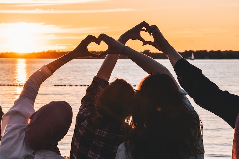 Foto: Junge Menschen bilden mit Händen Herzen vor Sonnenuntergang