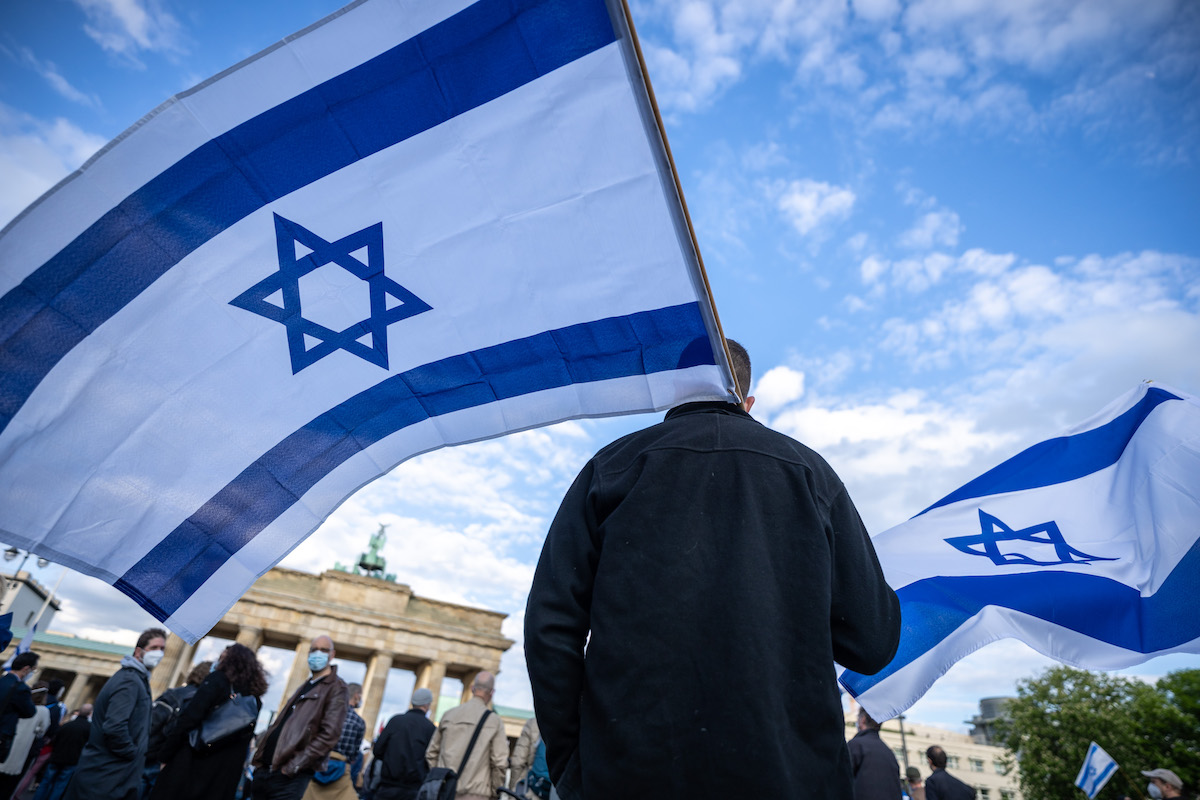 Foto: Teilnehmer an einer Demonstration zur Solidarität mit Israel stehen mit der Flagge Israels vor dem Brandenburger Tor.