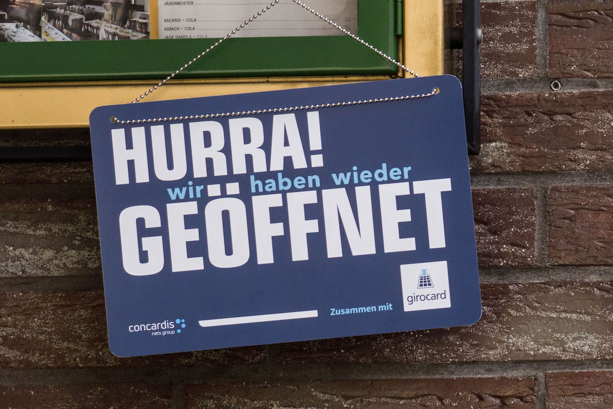 Foto: "Hurra! Wir haben wieder geöffnet" steht auf einem Schild unterhalb der Speisekarte einer Gaststätte. 