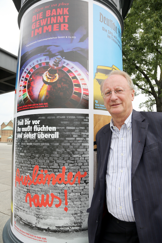 Foto: Klaus Staeck steht 2014 neben einer Litfaßsäule mit seinen Plakaten. 