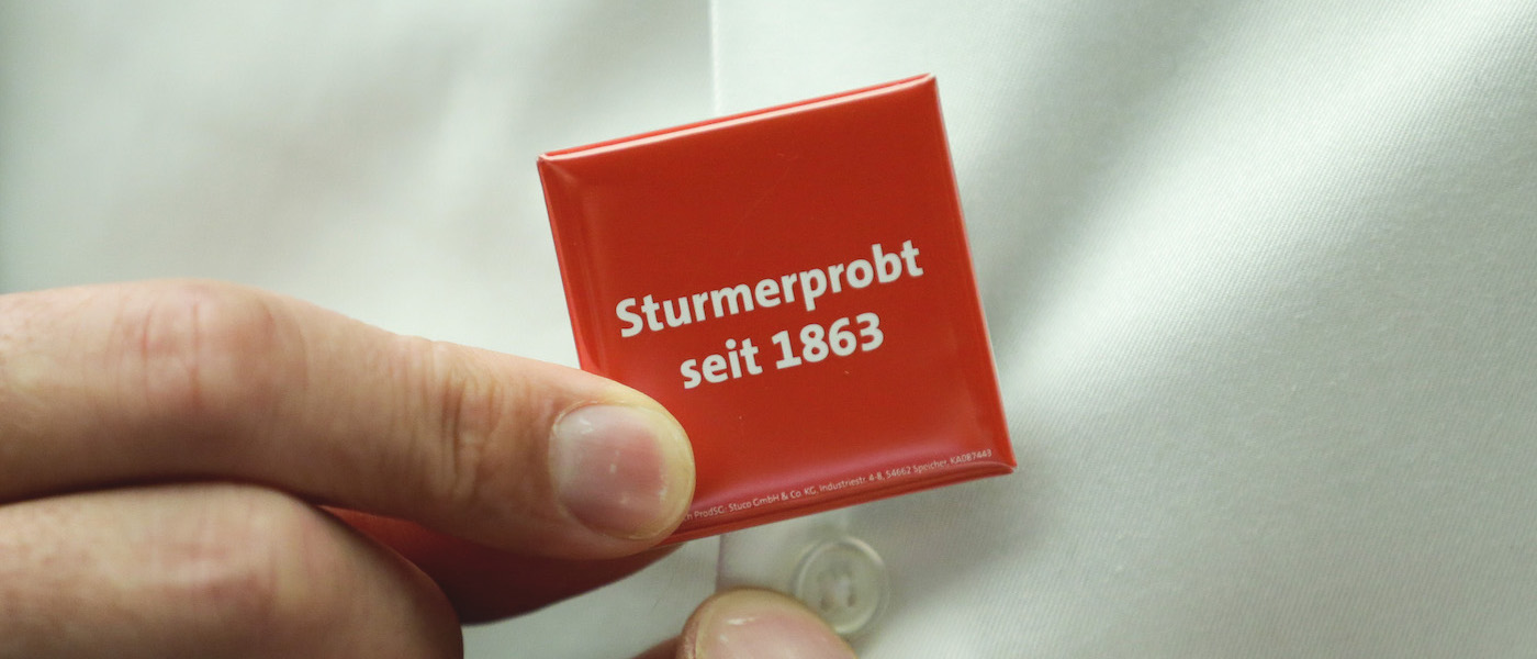 Foto: "Sturmerprobt seit 1863"-Sticker wird an Hemd geheftet