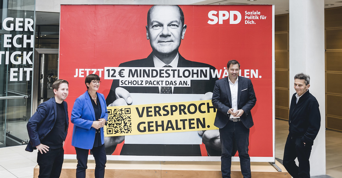 Foto: Die SPD-Parteispitze steht vor einem Mindestlohn-Plakat zur Bundestagswahl und klebt einen Störer "Versprochen. Gehalten."