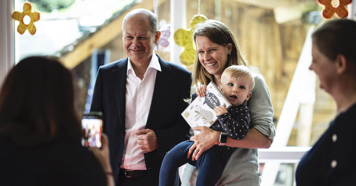 Foto: Olaf Scholz steht neben einer Frau, die ihr Kleinkind auf dem Arm hält