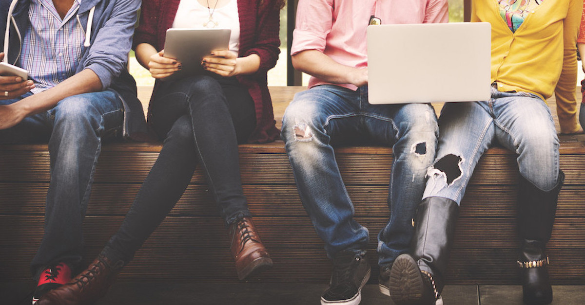 Foto: Junge Menschen sitzen nebeneinander mit Handy und Laptops