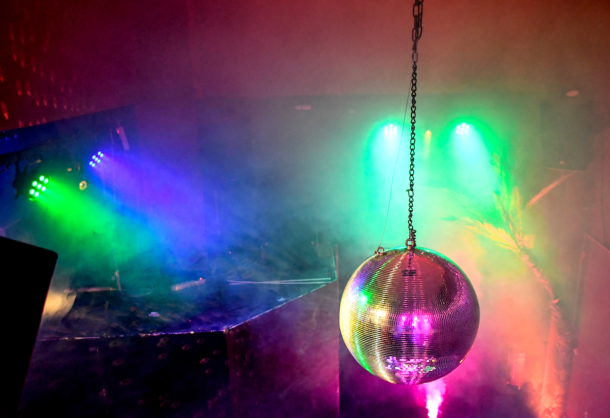 Foto: Eine Diskokugel dreht sich in einem Club und reflektiert das einfallende Licht der Scheinwerfer und Lampen. 