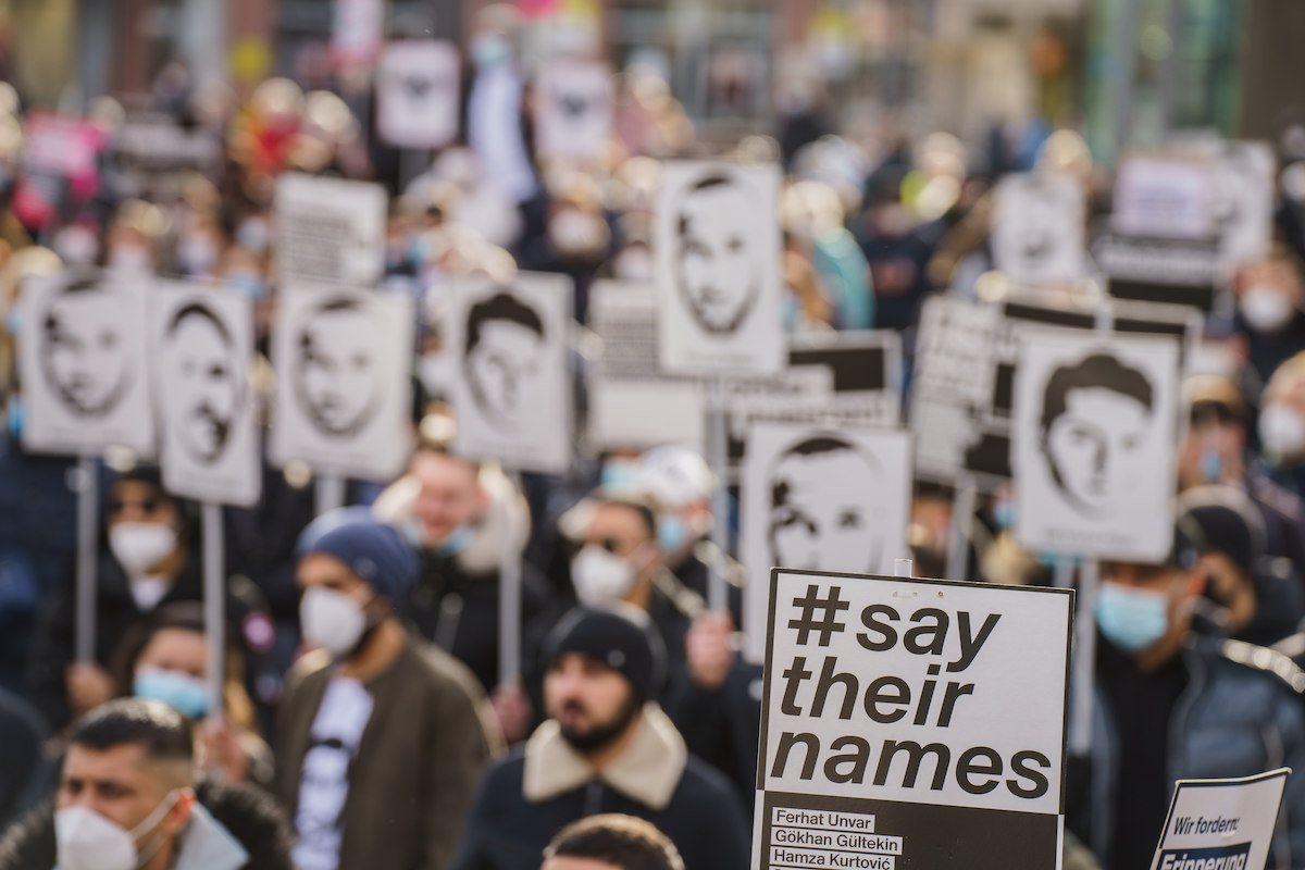 Foto: Ein Plakat „#say their names“ wird auf Gedenkkundgebung in Hanau hochgehalten. 