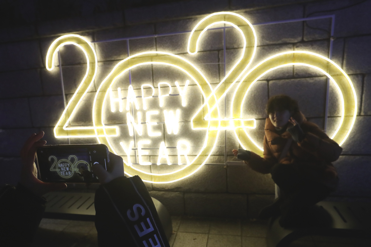 Foto: Eine Frau wird zum Jahreswechsel vor dem LED-Schriftzug "2020 Happy New Year" (Frohes Neues Jahr) fotografiert.