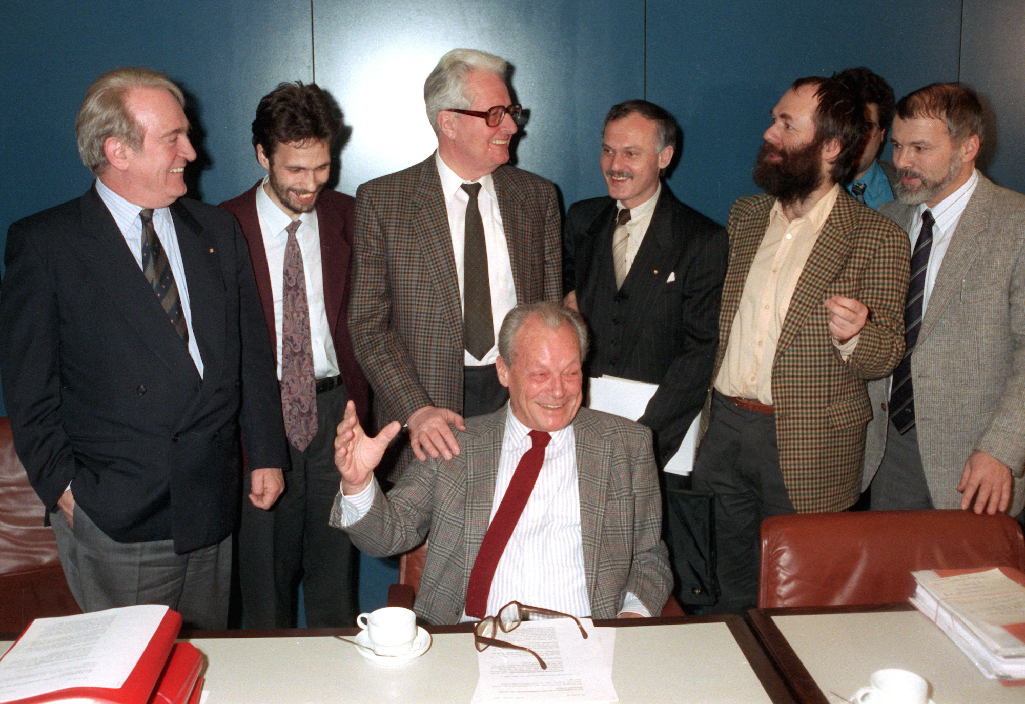 Foto: Stehend l-r Johannes Rau (SPD-West), Stephan Hilsberg (Sprecher der SPD-Ost), Hans-Jochen Vogel (Parteivorsitzender SPD-West), Ibrahim Böhme (Geschäftsführer SPD-Ost) und Markus Meckel (Zweiter Geschäftsführer der SPD-Ost), SDP-Gründungsmitglied Harald Ringstorff, sowie vorn sitzend Ex-Kanzler Willy Brandt (Ehrenvorsitzender SPD-West) sind auf ihrem gemeinsamen Treffen am 12. Februar 1990 in Bonn offensichtlich guter Dinge. 