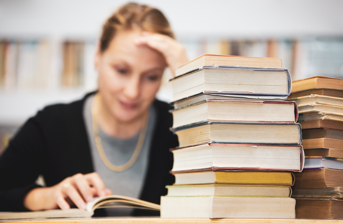 Foto: Studentin lernt hinter Bücherstapel