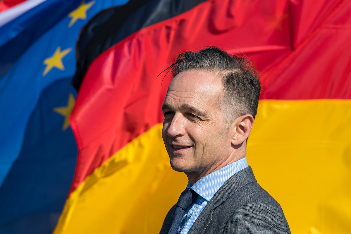 Foto: Heiko Maas steht vor den Flaggen Deutschlands und Europas.