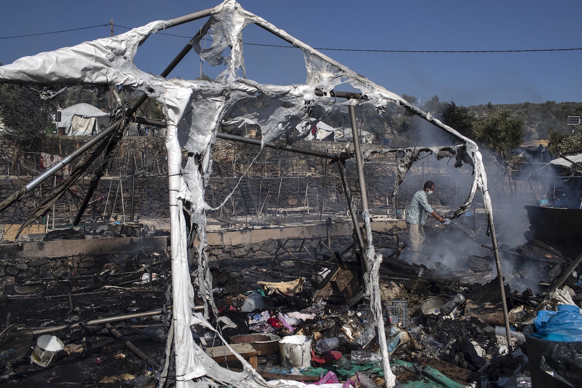 Foto: Ein Mann mit Mundschutz schüttet Wasser auf die Trümmer des Feuers im Lager Moria auf Lesbos, Griechenland