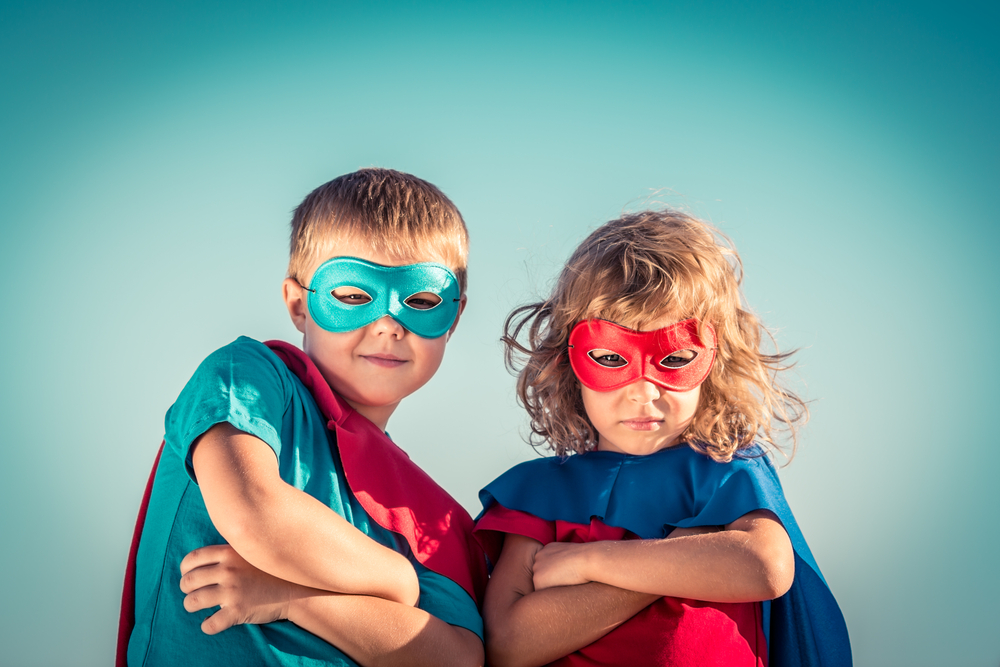 Foto: Ein Junge und ein Mädchen in Superman-Kostümen schauen die Arme verschränkt den Betrachter an.