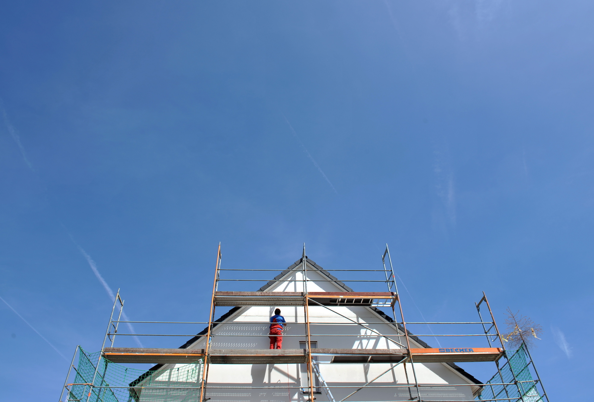 Foto: Ein Arbeiter ist an einer Fassade eines neuen Hauses beschäftigt.