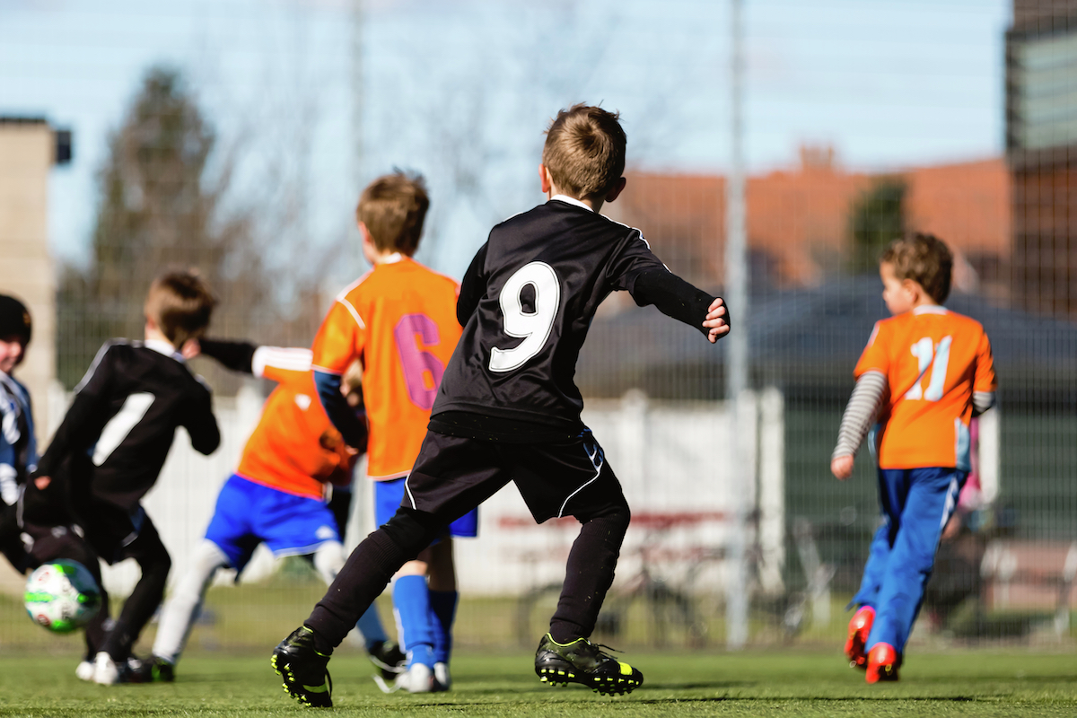 Foto: Kinder spielen auf einem Sportplatz Fußball