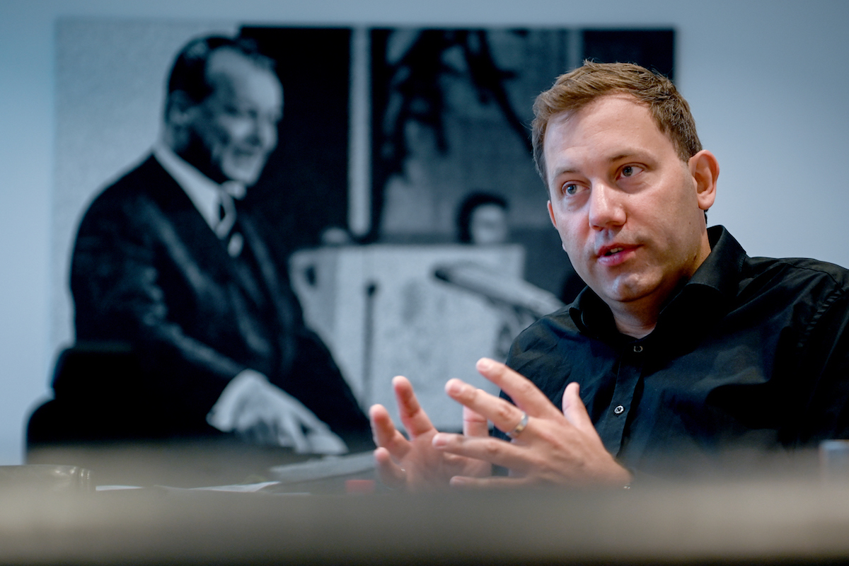 Foto: Lars Klingbeil spricht im Interview, im Hintergrund eine Fotografie des früheren Bundeskanzlers Willy Brandt.