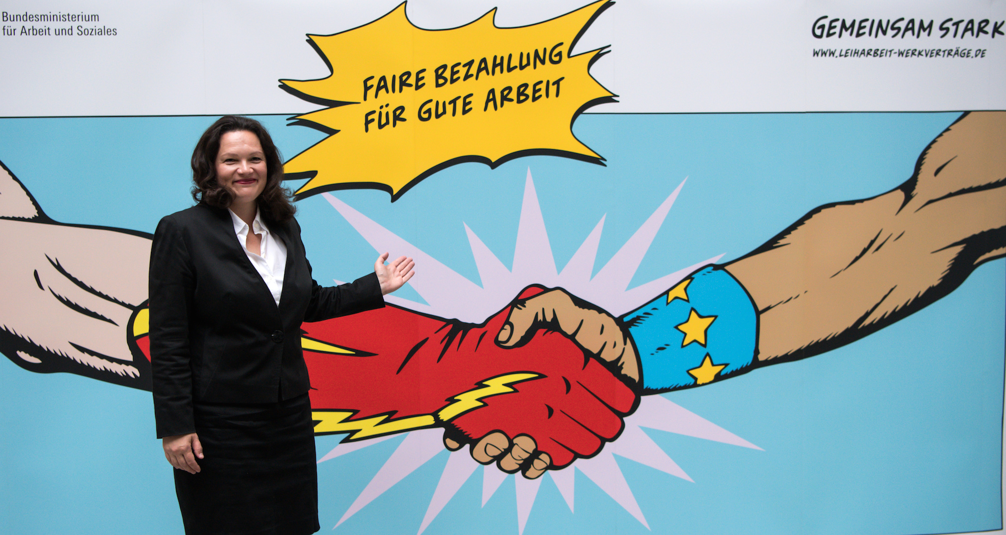 Foto: Andrea Nahles steht vor einem Plakat mit der Aufschrift "Faire Bezahlung für gute Arbeit"