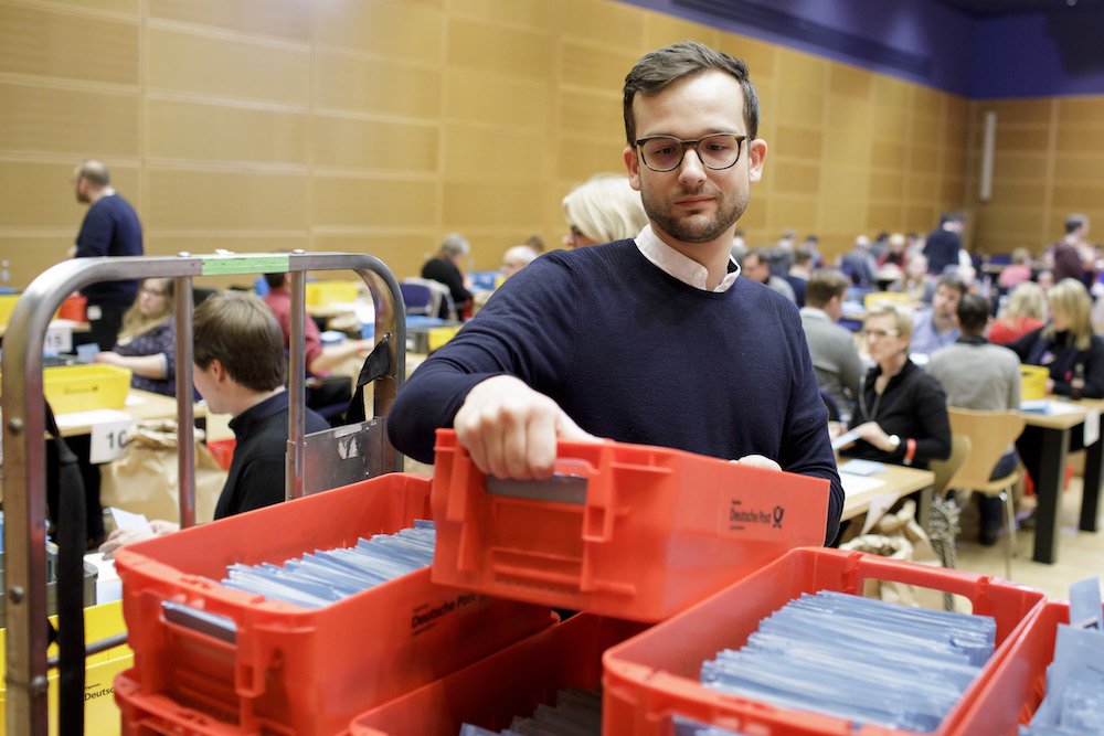 Foto: Ein Freiwilliger nimmt ein Kasten mit Stimmunterlagen zur Auszählung