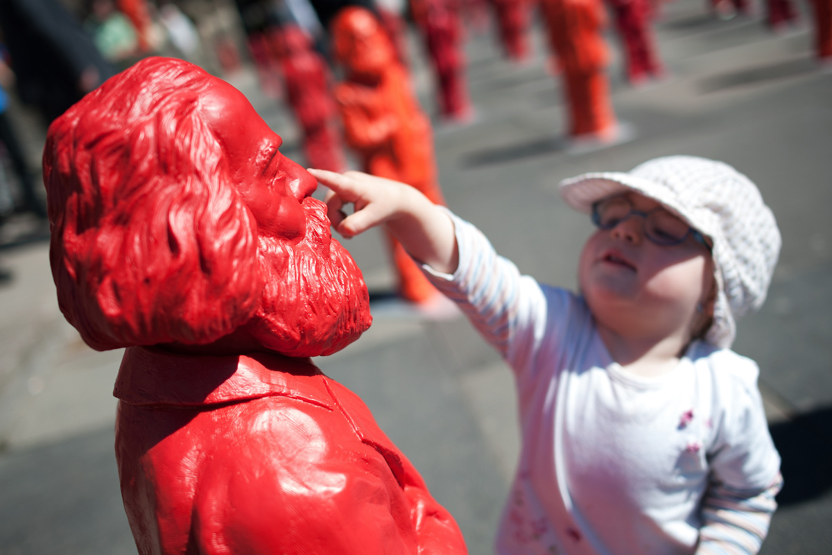 Foto: Ein kleines Mädchen greift einer Karl-Marx-Figur an die Nase.