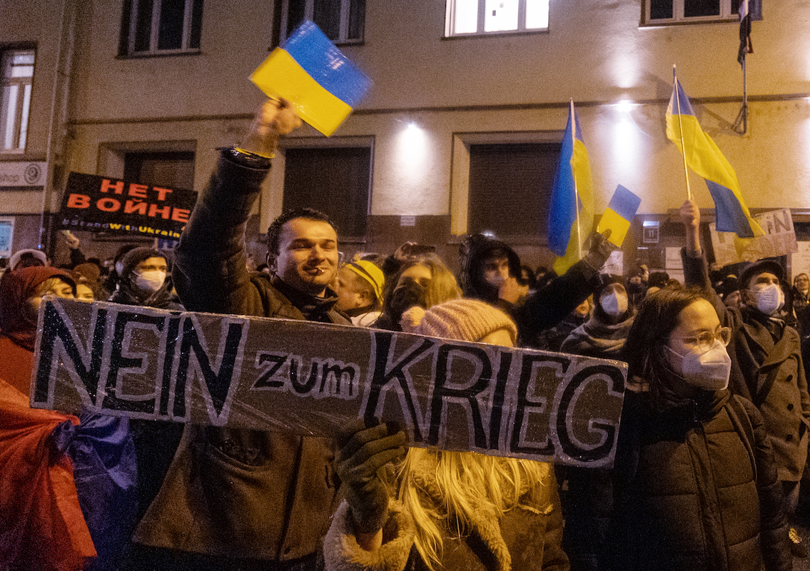 Foto: Menschen stehen bei einer Demonstration zur Unterstützung der Ukraine, nach dem russischen Angriff auf das Land, mit Schildern und ukrainischen Fahnen vor dem russischen Generalkonsulat in Frankfurt am Main