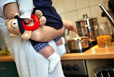 Foto: Eine Mutter hält beim Kochen ihr Kleinkind auf dem Arm.