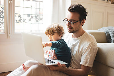 Foto: Vater sitzt mit Kind am Laptop