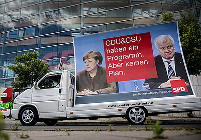 Foto: SPD-Kampagnenwagen fährt vor der CDU-Zentrale in Berlin vorbei, auf dem Plakat ist die Aufschrift "CDU & CSU haben ein Programm. Aber keinen Plan" zu lesen.