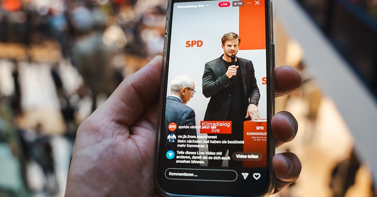 Foto: Robin Mesarosch spricht beim Klimadialog live, zu sehen auf einem Smartphone-Bildschirm