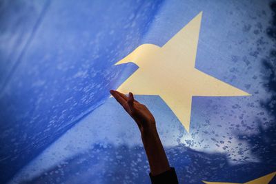 Foto: Eine Hand berührt eine überdimensionale Europaflagge
