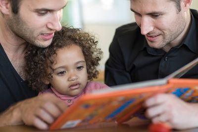 Bild: Zwei Männer lesen ein Buch mit einem Kind