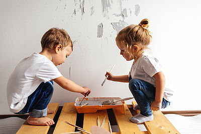 Foto: Junge und Mädchen pinseln an einer Wand